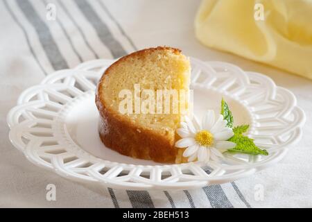 Une tranche de gâteau de limote ricotta moite sur une plaque décorative blanche avec une garniture de Marguerite et de feuilles de menthe. Banque D'Images