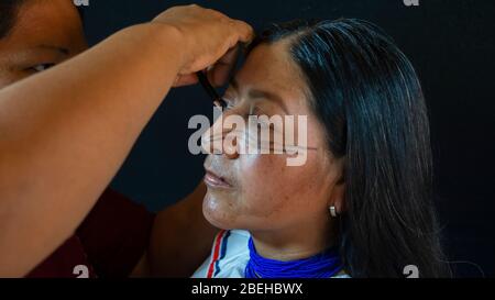 Femme du groupe ethnique de Quichua de l'Amazonie équatorienne qui applique le maquillage au visage de sa sœur en robe traditionnelle sur fond noir Banque D'Images