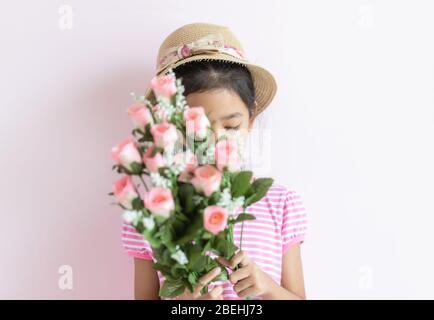 Portrait d'une petite fille asiatique portant une robe rayée rose et blanche. L'enfant porte un chapeau et tient un bouquet de fleurs couvrant son visage. Sélectionnez Banque D'Images