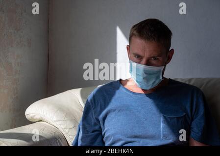 L'homme est assis par une fenêtre isolée portant un masque facial pendant la pandémie de Covid-19 de 2020 Banque D'Images