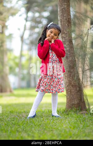 Petite fille en robe de fleur et pull rouge, très heureux et souriant dans la forêt Banque D'Images