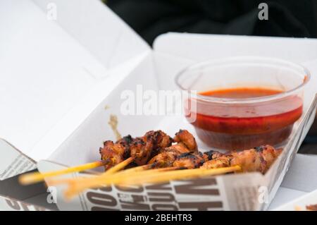 Gros plan de viande barbecue sur une brochette avec sauce Chili dans un récipient à emporter en papier. Scène de restauration rapide. Mise au point sélective Banque D'Images