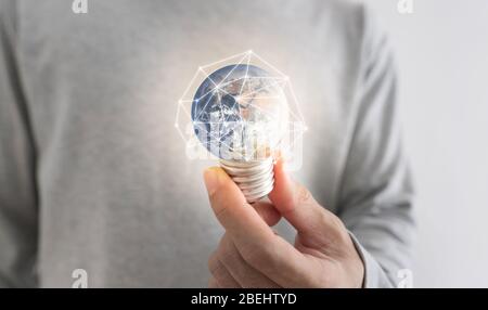 Économie d'énergie et concept de jour de terre. Un homme qui tient une ampoule de terre lumineuse. L'élément de cette image est fourni par la NASA Banque D'Images