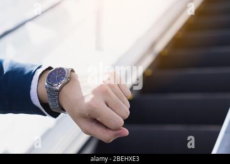 La photo de gros plan de l'homme d'affaires regardant sa montre dans sa main tout en se tenant sur l'escalator. Concept d'affaires et de finances. Banque D'Images