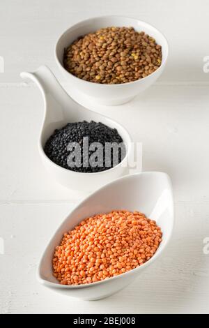 Différents lentilles assorties se mélangent avec des lentilles béluga rouges, brunes et noires dans des bols blancs sur fond de table en bois blanc - foyer sélectif Banque D'Images