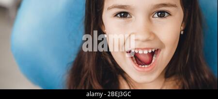 Une jeune fille caucasienne heureuse avec un sourire à la bouche ouvert à l'appareil photo après un examen des dents chez le dentiste pédiatrique Banque D'Images