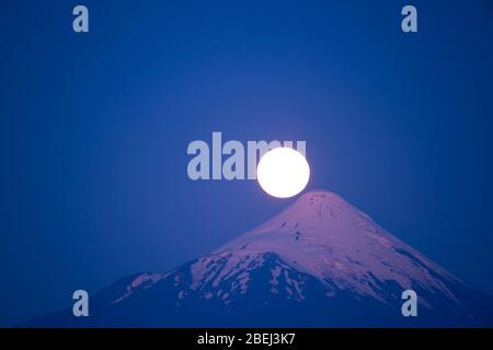 Pleine lune se levant à côté du sommet du volcan Osorno après le coucher du soleil avec les couleurs de l'heure bleue Banque D'Images