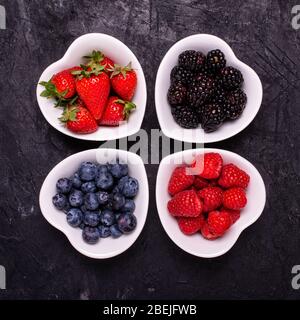 dans les quatre bols blancs en céramique en forme de coeur, baies mûres, au premier plan, contre le fond sombre Banque D'Images