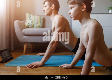 Jeune homme avec son fils faisant du yoga à la maison en quarantaine. Père et fils en haut faisant face à l'asana de chien Banque D'Images