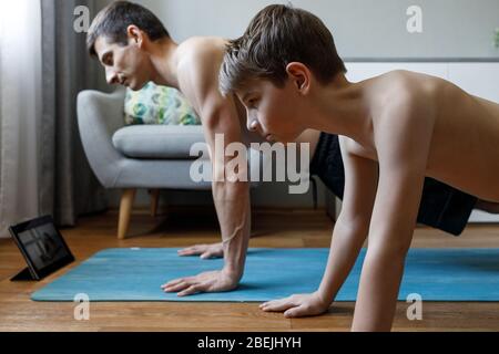 Jeune homme avec son fils faisant du yoga à la maison en quarantaine. Banque D'Images