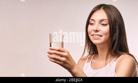 Jeune fille magnifique qui tient du verre d'eau. Hydrate visage femelle. Les femmes heureuses à l'intérieur