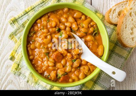 Haricots blancs avec tranches de saucisse dans la sauce tomate et persil dans un bol vert avec cuillère sur une table en bois. Le haricot est la source de protéines végétales. Banque D'Images