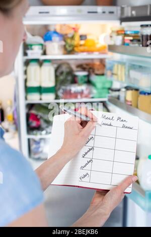 Femme debout devant le réfrigérateur dans la cuisine avec carnet écriture repas hebdomadaire Banque D'Images