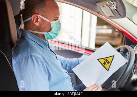 Automobiliste avec masque facial et avertissement de risque biologique sur une feuille de papier Banque D'Images