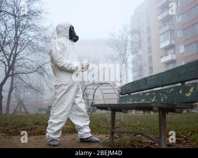 Scientifique dans le masque à gaz et de protection de l'environnement urbain de surveillance des vêtements, tenant des brucelles. De la vue ci-dessous de l'homme debout près de la banquette sur le terrain de jeu. Catastrophe environnementale, atmosphère fumée vide. Banque D'Images