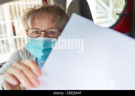 Une femme âgée avec masque facial est titulaire d'une feuille de papier vierge pour obtenir des informations sur l'épidémie de Covid-19 et de Coronavirus Banque D'Images