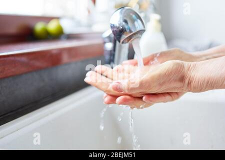 Vieille femme se laver les mains avec du savon sous le robinet de l'évier Banque D'Images