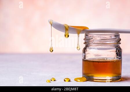 au premier plan, des gouttes de miel de châtaignier biologique provenant de la cuillère en céramique blanche tombent sur la surface de la structure grise Banque D'Images
