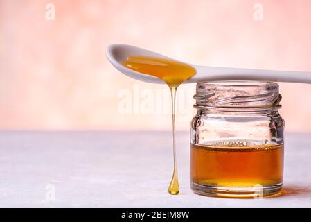 au premier plan, des gouttes de miel de châtaignier biologique provenant de la cuillère en céramique blanche tombent sur la surface de la structure grise Banque D'Images