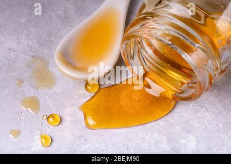 au premier plan, le miel de châtaignier biologique est versé du pot en verre inversé sur la structure grise Banque D'Images