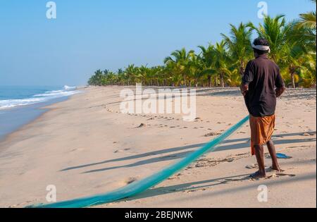 Pêcheur se tenant sur la belle plage de Marari en début de matinée à la pêche avec un filet de coulage vert à la main - Mararikulam, Alapuzha District, Kerala, Inde Banque D'Images