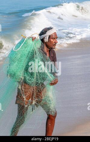 Pêcheur en début de matinée portant un filet de coulée à main verte sur la belle plage de Marari, Mararikulam, Alapuzha District, Kerala, Inde Banque D'Images