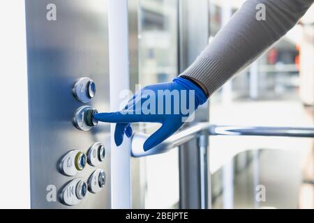 La main dans un gant en caoutchouc appuie sur le bouton de l'élévateur ou du relevage. Protection personnelle contre les germes, les bactéries et les virus : porter des gants de main en place Banque D'Images