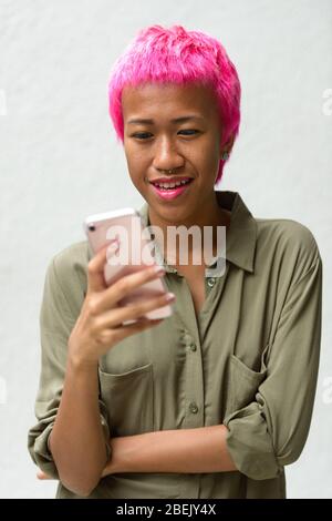 Heureuse jeune femme rebelle asiatique avec des cheveux roses en utilisant le téléphone Banque D'Images