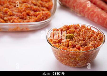 Gajar ka halwa dans un bol en verre maintenu devant les carottes et un bol de service. Banque D'Images