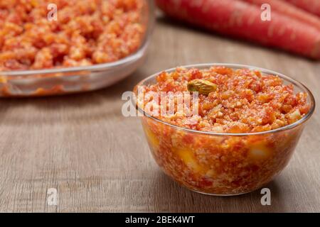 Gajar ka halwa dans un bol en verre maintenu devant les carottes et un bol de service. Banque D'Images