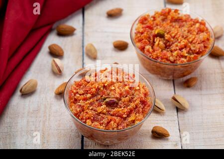 Deux bols de gajar ka halwa gardaient sur une table en bois avec des fruits secs dispersés dessus. Banque D'Images