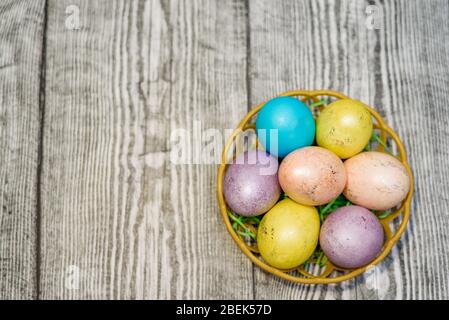 Un panier avec de nombreux œufs de pâques multicolores sur le fond gris en bois. Espace pour le texte. Vacances de Pâques. Banque D'Images
