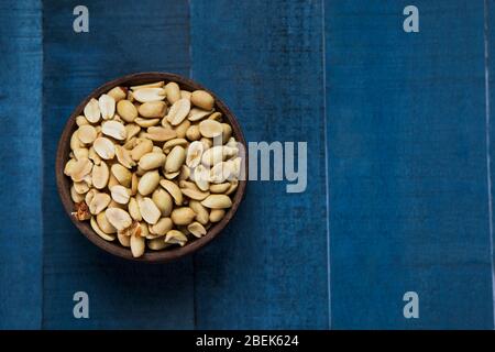 Arachides simples gardées dans un bol en bois sur une table en bois bleu. Banque D'Images
