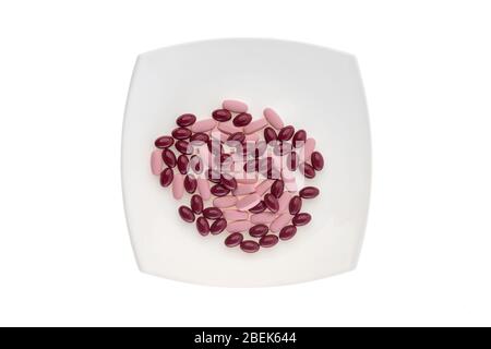 Une pile de pilules sur une plaque blanche symbolisant la nourriture. Vitamines sur fond blanc isolé. Pilules roses et gels bordeaux. Repas de prescription Banque D'Images