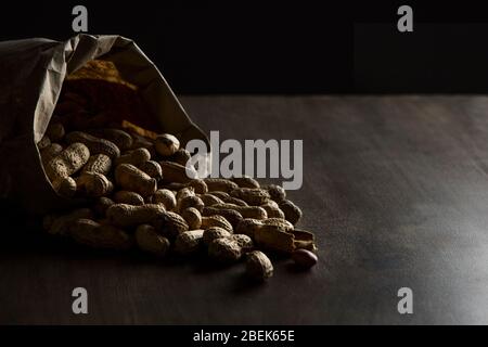 Arachides rôties sortant d'un sac en papier marron sur une table en bois. Banque D'Images