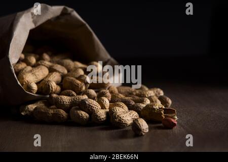 Arachides rôties sortant d'un sac en papier marron sur une table en bois. Banque D'Images