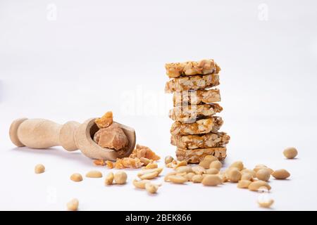 La quincaillerie dans une cuillère en bois gardée avec mungfali chikki et des arachides sur fond blanc. Banque D'Images