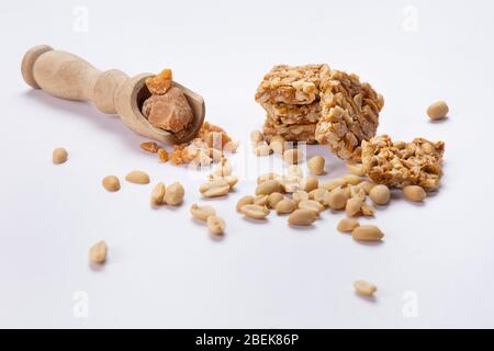 La quincaillerie dans une cuillère en bois gardée avec mungfali chikki et des arachides sur fond blanc. Banque D'Images