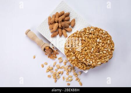 La quincaillerie dans une cuillère en bois avec des arachides pleines gardées avec du chikki et des arachides sur un plateau blanc Banque D'Images