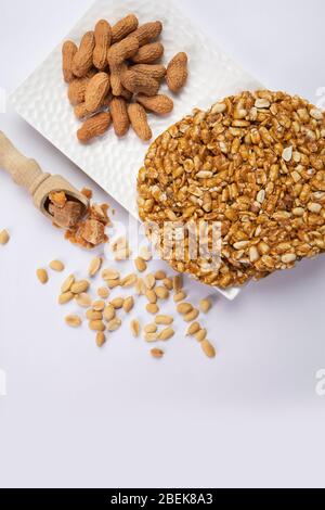 La quincaillerie dans une cuillère en bois avec des arachides pleines gardées avec du chikki et des arachides sur un plateau blanc Banque D'Images