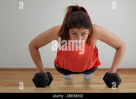 Femme faisant des poussettes avec des haltères sur un plancher en bois. Banque D'Images