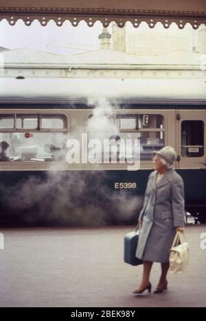 1970, vieille dame avec étui de costume, voyageant seul, scène sur British Railways, Royaume-Uni, Huddersfield station, West Yorkshire Banque D'Images