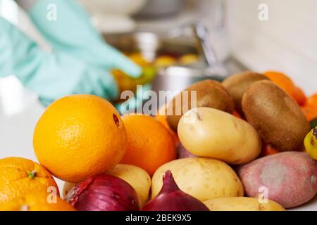 gros plan d'un homme dans la cuisine, porter des gants, laver quelques fruits et légumes fraîchement achetés, sur l'évier avec de l'eau et de l'aseptisant alimentaire Banque D'Images