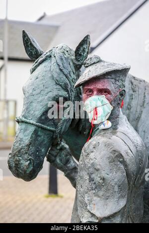 Irvine, Royaume-Uni. 14 avril 2020. La statue emblématique du carter et de son cheval Clydesdale au port d'Irvine représente les connexions nationales et internationales de la ville et sa résilience aux difficultés. Maintenant quelqu'un avec un sens de l'humour a mis un masque PPE sur le carter pour empêcher la contagion de Covid 19, peint son visage et a laissé une pierre peinte sur son épaule remerciant le NHS. Crédit: Findlay/Alay Live News Banque D'Images