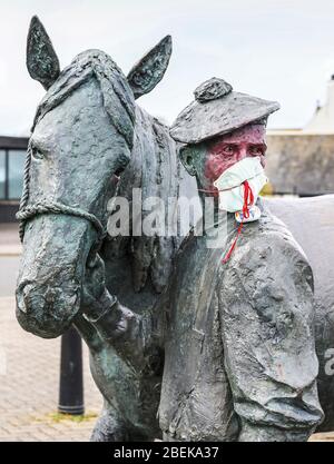 Irvine, Royaume-Uni. 14 avril 2020. La statue emblématique du carter et de son cheval Clydesdale au port d'Irvine représente les connexions nationales et internationales de la ville et sa résilience aux difficultés. Maintenant quelqu'un avec un sens de l'humour a mis un masque PPE sur le carter pour empêcher la contagion de Covid 19, peint son visage et a laissé une pierre peinte sur son épaule remerciant le NHS. Crédit: Findlay/Alay Live News Banque D'Images