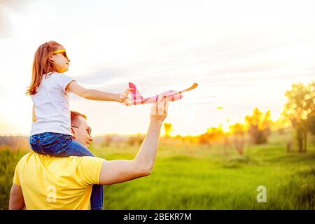 Homme gai souriant et portant une fille excitée sur les épaules tout en jouant avec des avions rouges ensemble contre ciel nuageux le jour ensoleillé de l'été Banque D'Images