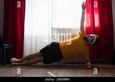 Homme joyeux faisant un exercice de planche latérale dans la chambre Banque D'Images