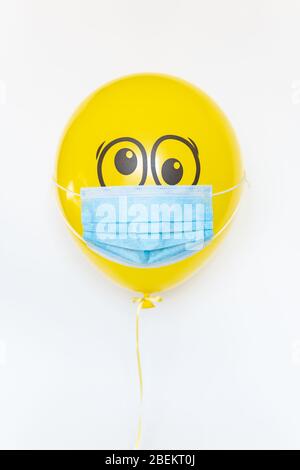 Ballon jaune avec masque médical et gribouille les yeux choqués. Image conceptuelle de la fête d'anniversaire pendant le verrouillage de quarantaine du virus Corona Banque D'Images