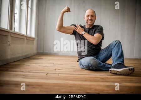 Homme souriant d'âge moyen assis sur le sol fléchit ses muscles Banque D'Images