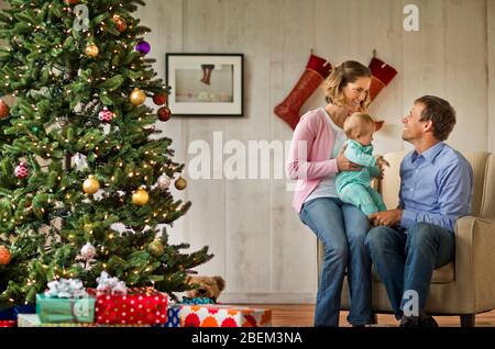 Couple adulte moyen et leur fille de bébé assis à côté d'un arbre de Noël Banque D'Images